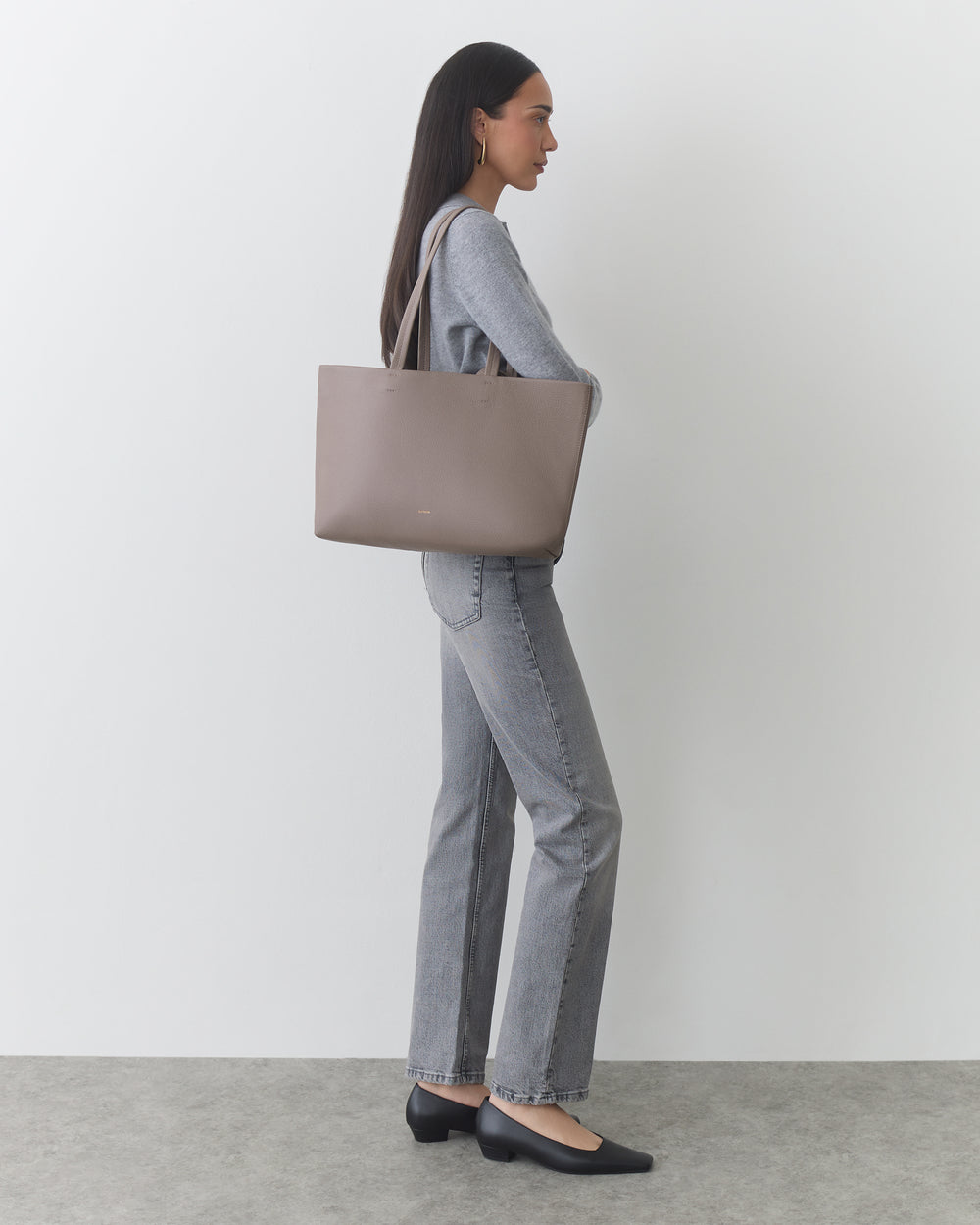 Person standing with large tote bag wearing jeans and shoes.