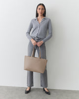 Person holding a handbag wearing a long-sleeve shirt and jeans.