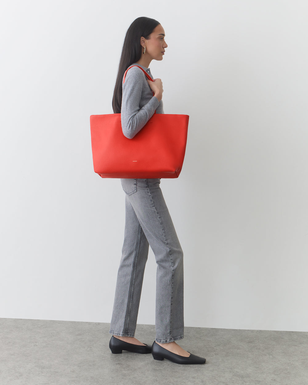 Person in profile view holding large tote bag, wearing long-sleeve shirt and jeans.