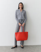 Person standing, holding large tote bag, wearing buttoned shirt and pants.