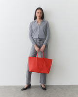 Person holding large tote bag standing against plain background.