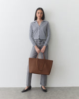 Person standing, wearing cardigan and jeans, holding a large tote bag.