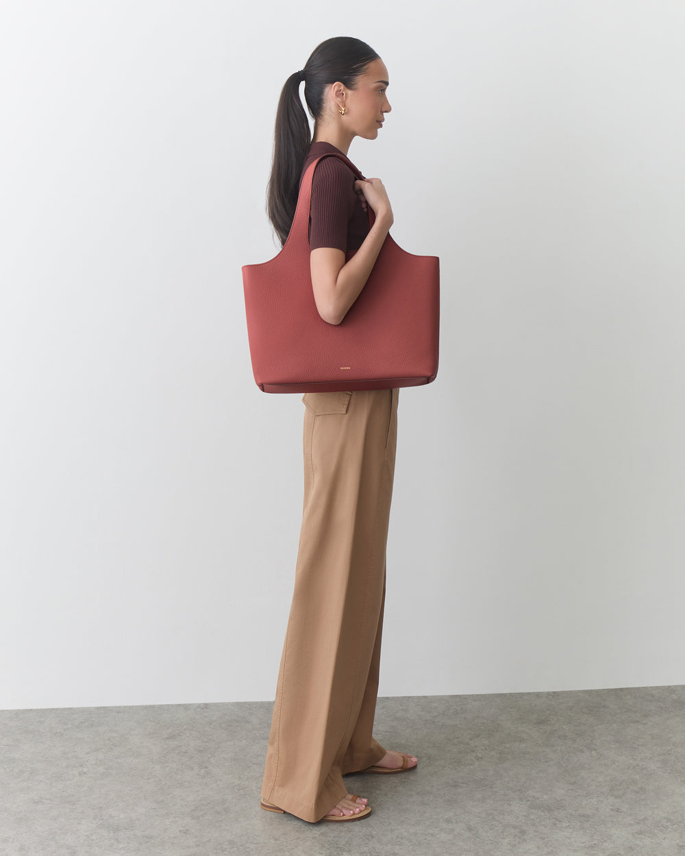 Person holding a large tote bag, standing sideways in casual clothing.