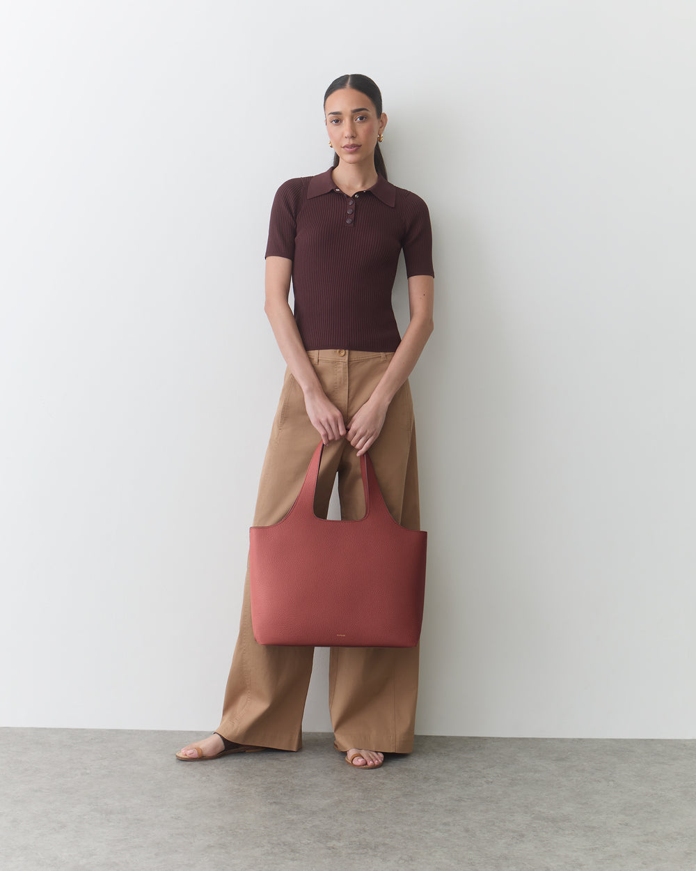 Person standing, wearing short-sleeved top, wide pants, holding large bag.