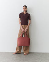 Person standing, wearing short-sleeved top, wide pants, holding large bag.