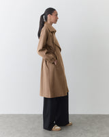 Person in a long coat and wide trousers stands sideways with hands in pockets.