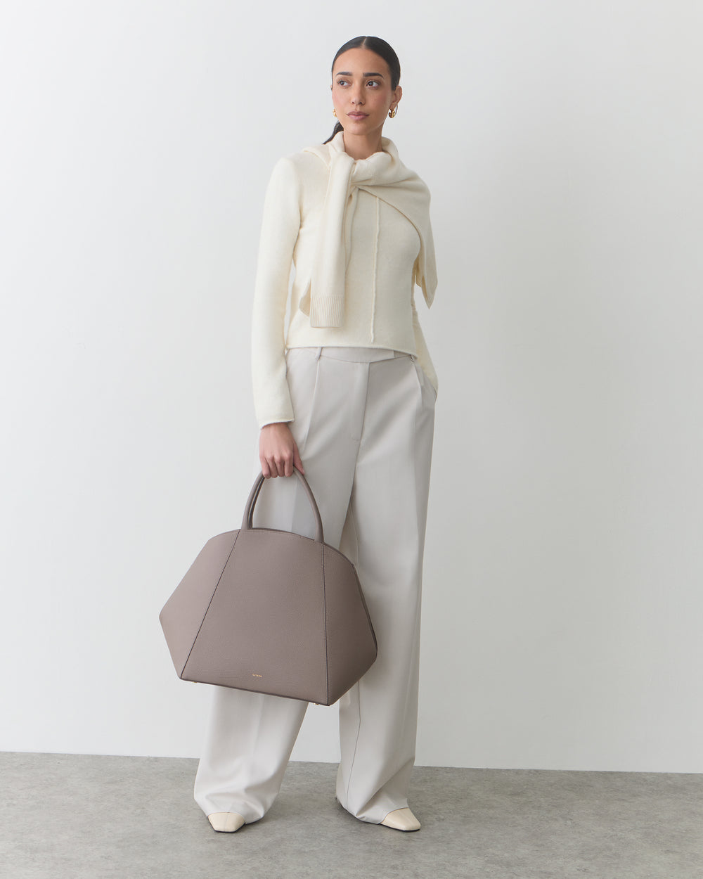 Person in a stylish outfit holding a large handbag standing indoors.