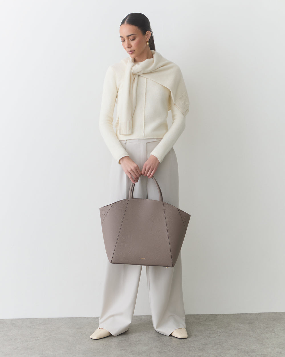 Person holding large tote bag, wearing sweater, pants, and shoes.