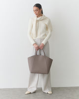 Person holding large tote bag, wearing sweater, pants, and shoes.