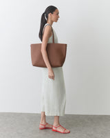 Person in a long dress carrying a large tote bag over the shoulder.