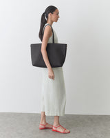 Person in a long dress carrying a large handbag, wearing sandals.