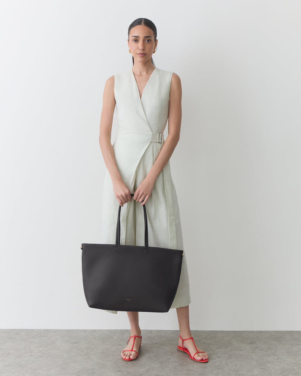 Person wearing a sleeveless dress holding a large shoulder bag, standing indoors.