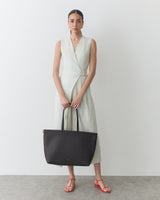 Person wearing a sleeveless dress holding a large shoulder bag, standing indoors.