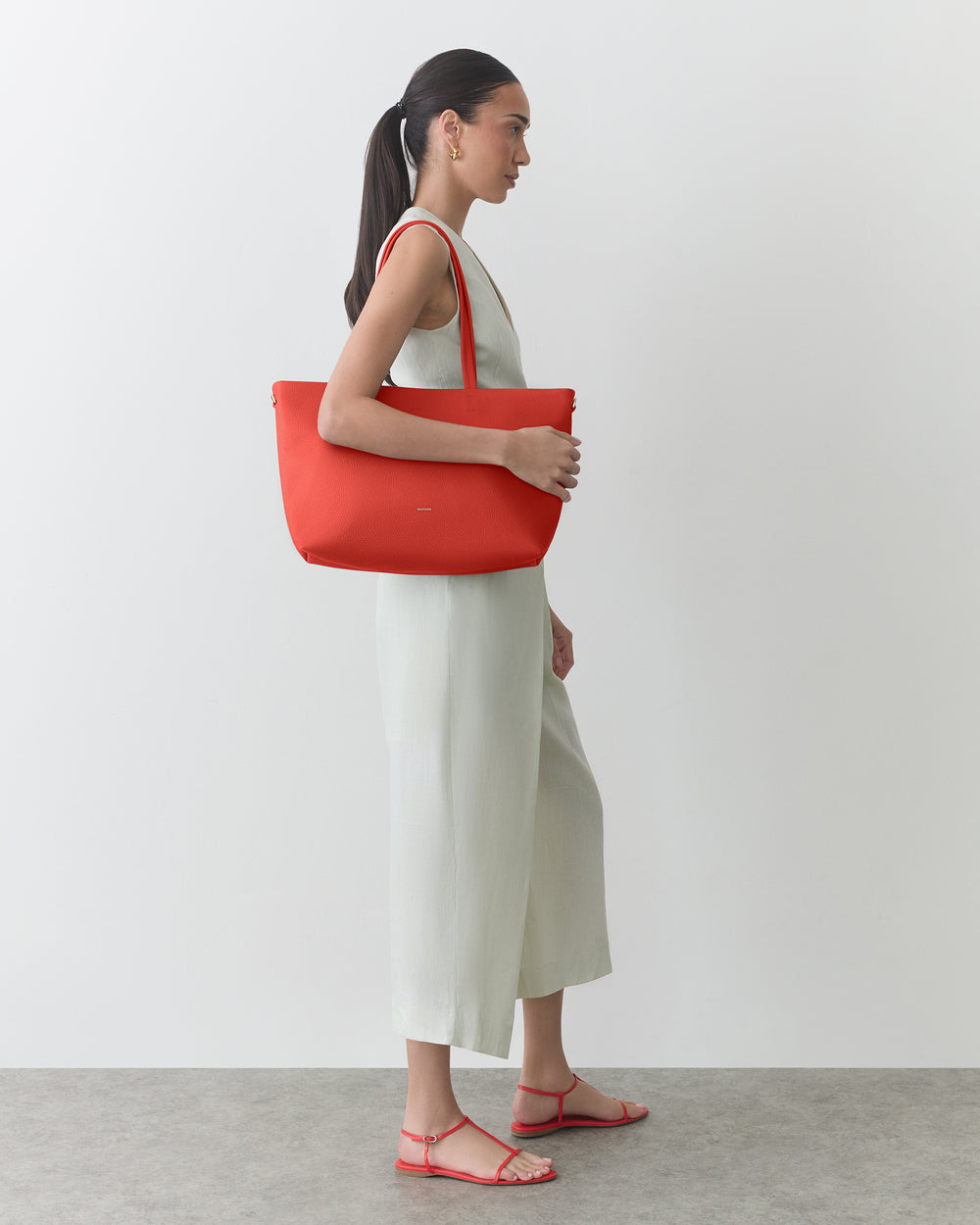 Person in a sleeveless jumpsuit carrying a large shoulder bag, standing sideways.