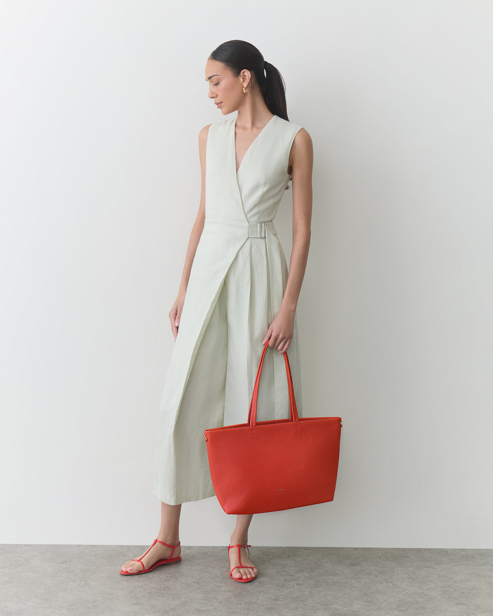 Person in a sleeveless dress holding a large tote bag, wearing sandals.