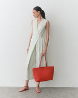 Person in a sleeveless dress holding a large tote bag, wearing sandals.