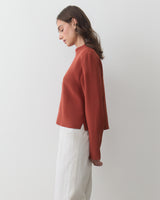 Person in profile wearing a long-sleeve top and pants standing against a plain background.