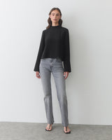 Person in long-sleeve top and jeans, standing on a plain floor.