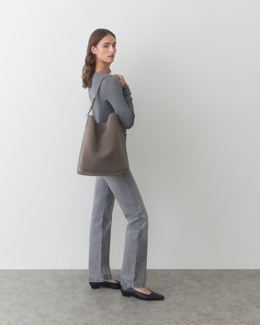 Person carrying shoulder bag, wearing long-sleeve shirt and pants, standing sideways.