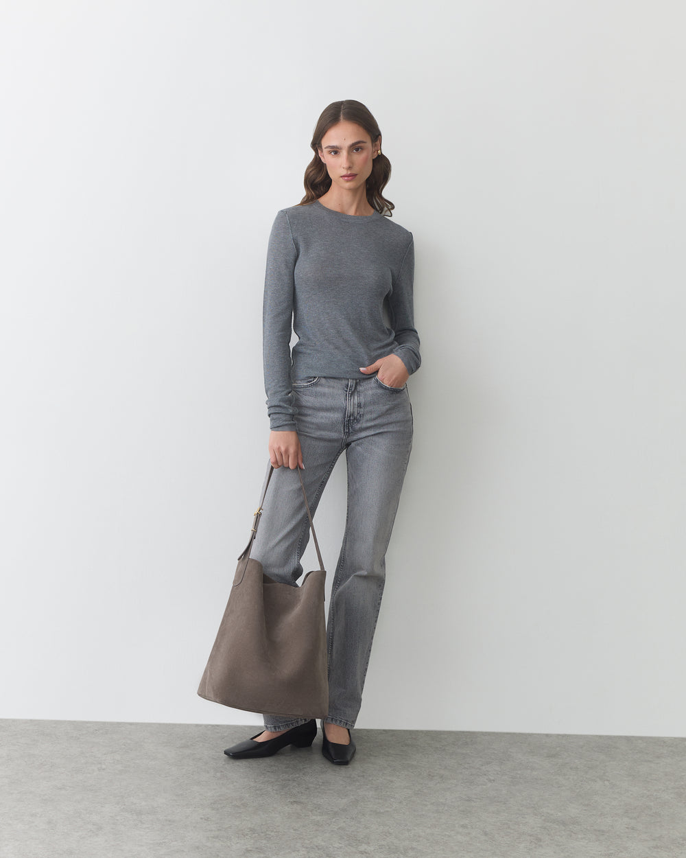 Person standing with a large bag wearing a long-sleeve shirt and jeans.