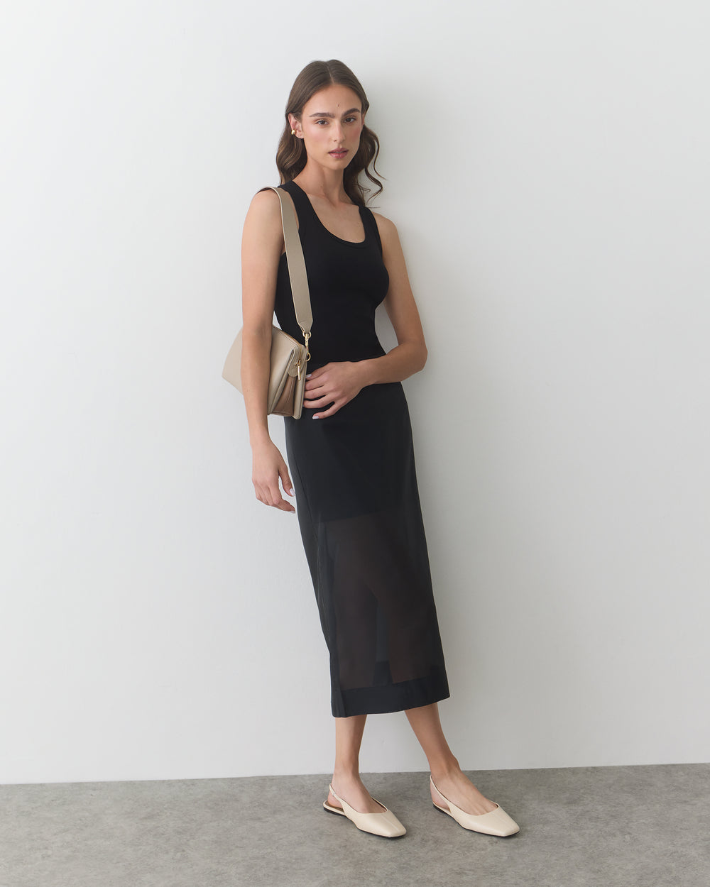 Person in dress holding a handbag standing against a wall