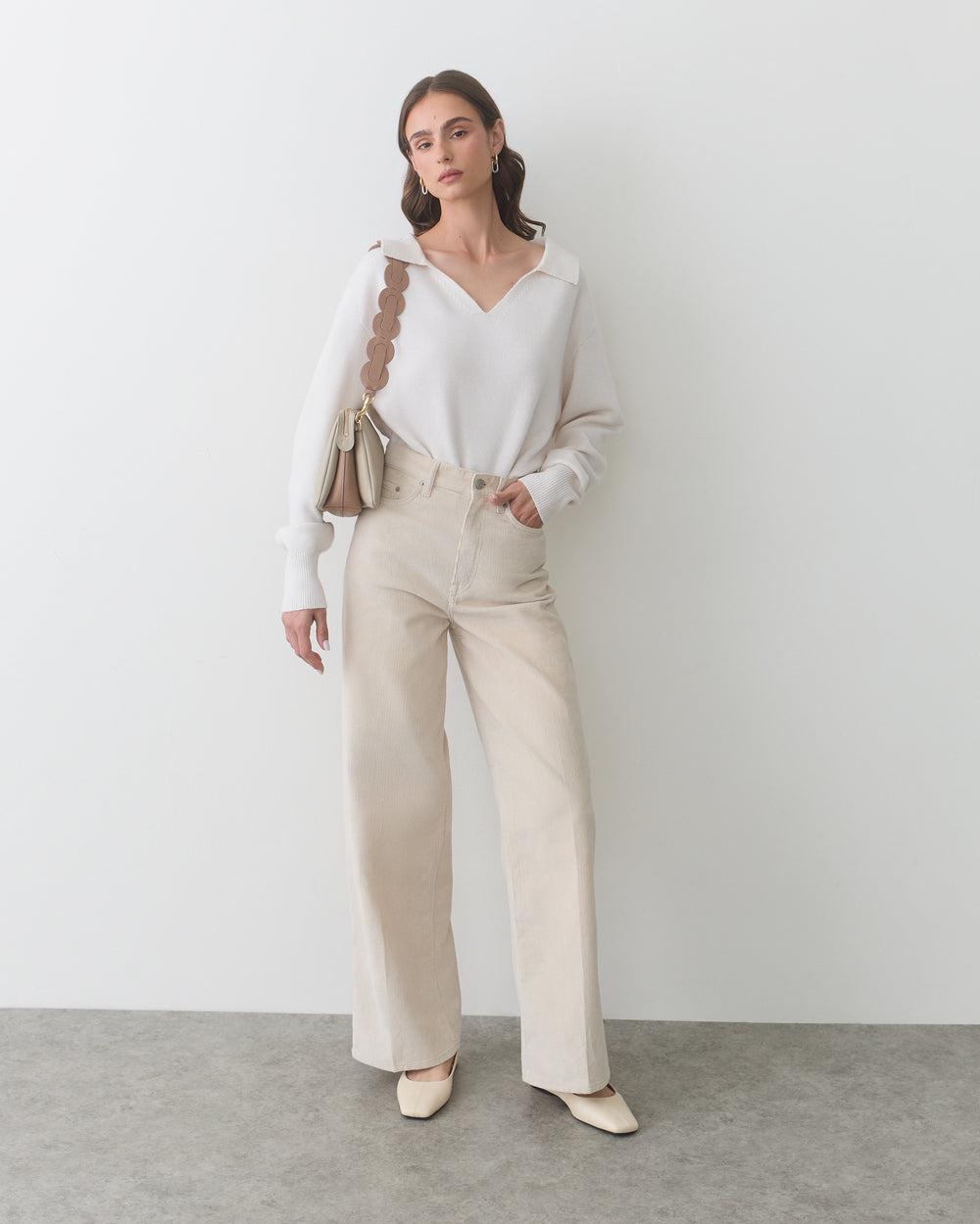 Model wearing sweater and wide-leg pants, holding a bag with a scalloped strap.