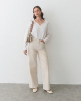 Model wearing sweater and wide-leg pants, holding a bag with a scalloped strap.