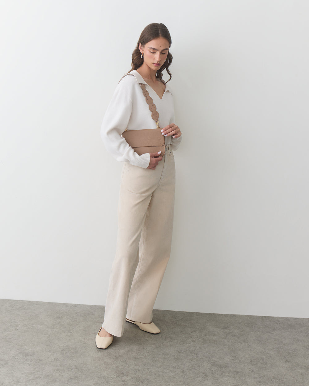 Woman standing with a belt bag over her shoulder, wearing pants and a top.