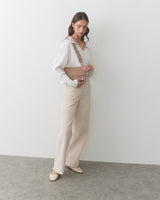 Woman standing with a belt bag over her shoulder, wearing pants and a top.