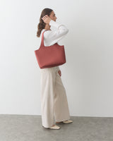 Person carrying a large tote bag, wearing a sweater and wide-leg pants.