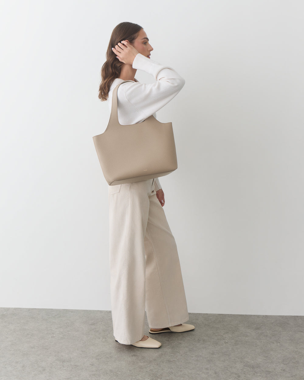 Person in white outfit carrying a large bag, standing against a plain background.