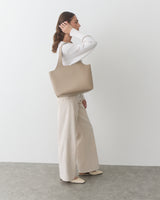 Person in white outfit carrying a large bag, standing against a plain background.