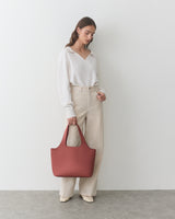 Person holding a tote bag, dressed in a top and pants, standing indoors.