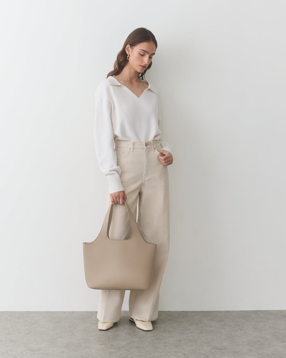 Person holding a large handbag, wearing a long-sleeve top and wide-leg pants.