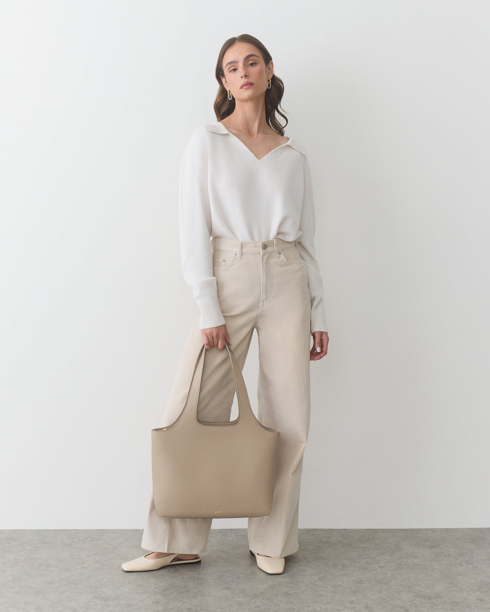 Person wearing a sweater and pants, holding a large tote bag.