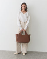 Person standing with a large tote bag in hand against a plain background.