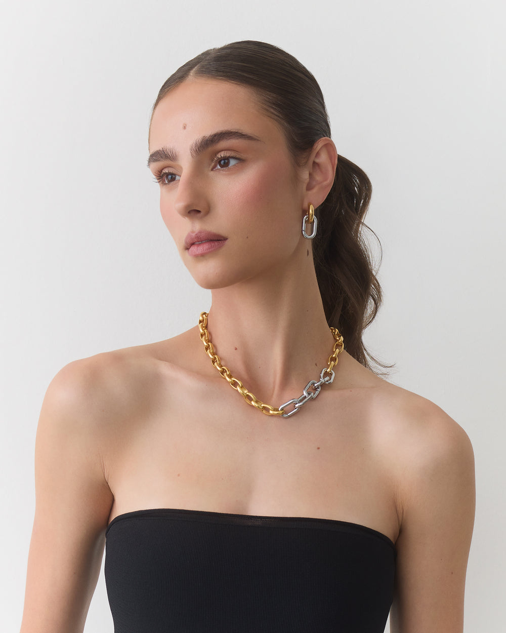 Person wearing a strapless top, gold and silver chain necklace, and hoop earrings.