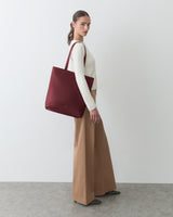 Person standing with large tote bag on shoulder, wearing long pants and long-sleeve top.