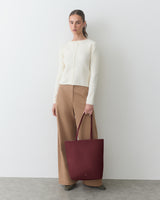Person standing with a large tote bag wearing a sweater and wide-leg pants.