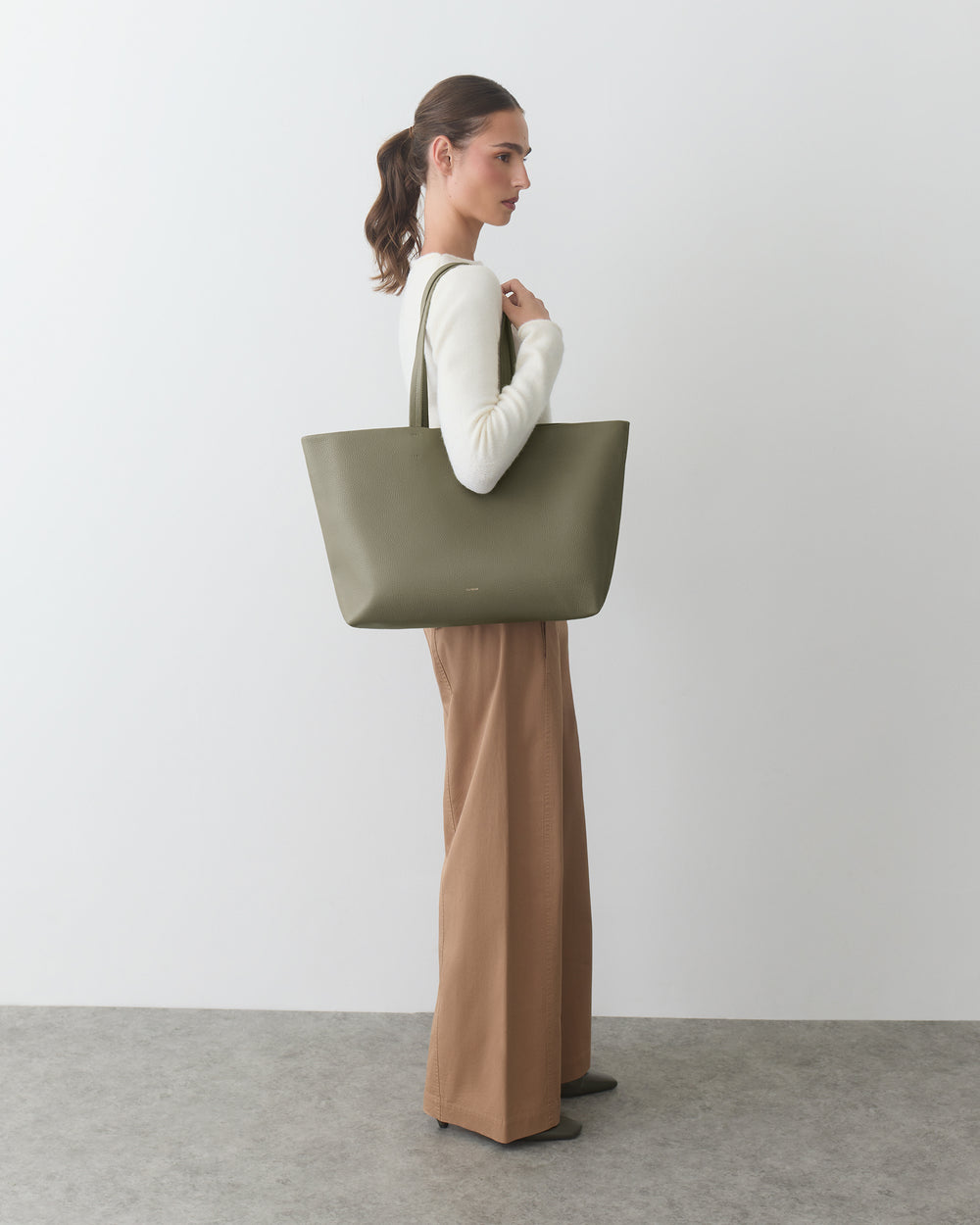 Person holding a large handbag and wearing a long-sleeve top with wide-legged pants.