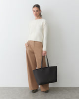 Person wearing sweater and pants holding large tote bag.