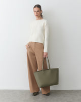 Person wearing a sweater and pants, holding a large handbag.