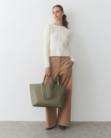 Woman standing with a large handbag, wearing a long-sleeve top and wide-leg pants.