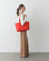 Person standing with large shoulder bag, wearing long-sleeve top and wide-leg pants.