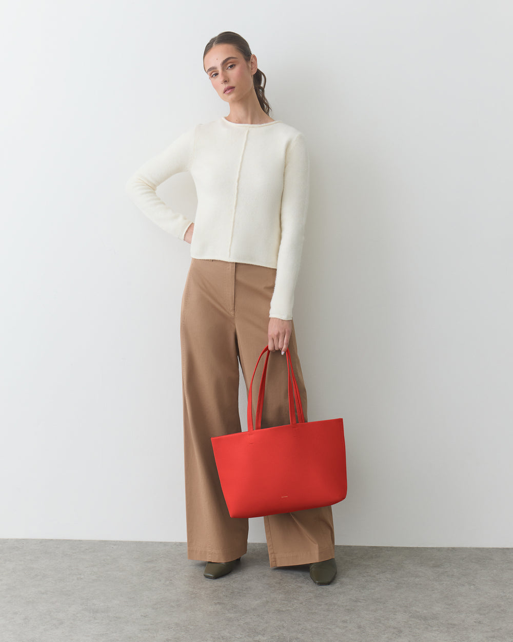 Person holding a red tote bag, wearing a long-sleeve top and wide-leg pants.