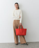 Person holding a large tote bag, wearing a long-sleeve top and wide-leg pants.