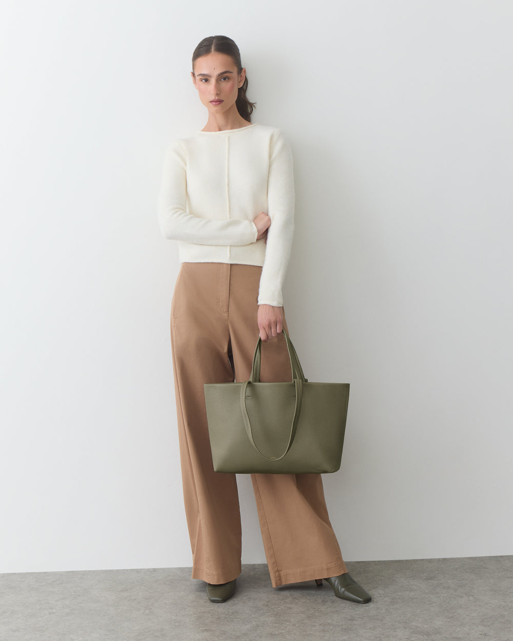 Person in a plain top and wide pants holding a handbag.
