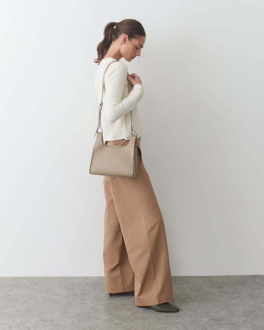 Person in a side pose holding a shoulder bag, wearing a sweater and wide-leg pants.
