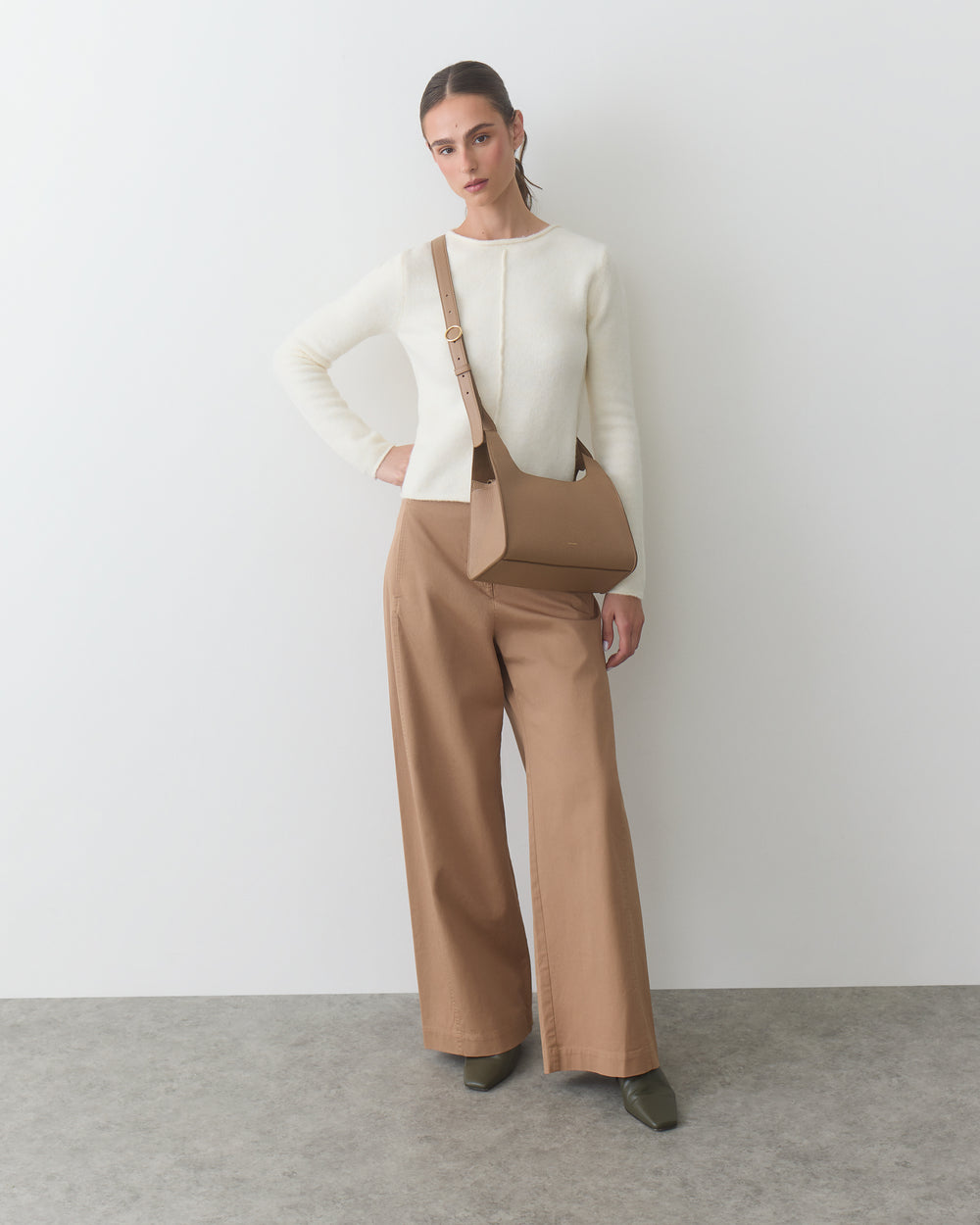 Person in long-sleeve top and wide-leg pants, holding a shoulder bag.