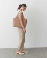 Person standing with large shoulder bag, wearing sleeveless top and pants.